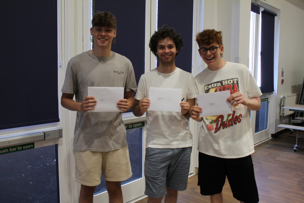 Three male Post-16 students are pictured smiling for the camera together in a hall, after having just opened their A-Level results.